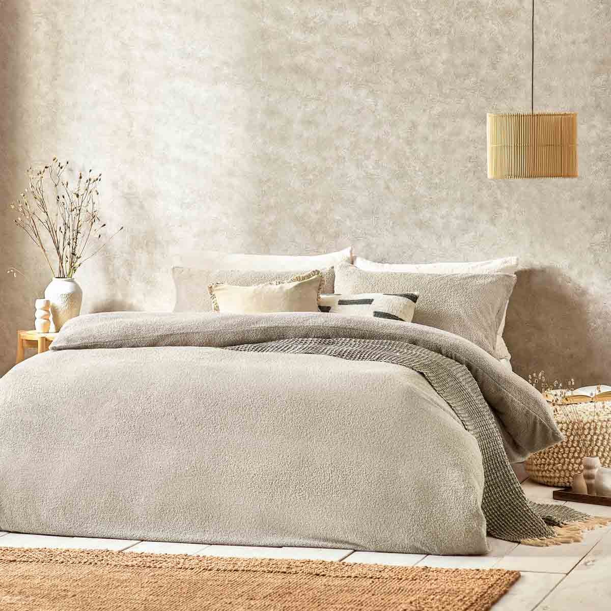 Beige boucle textured duvet set featuring a soft, cozy fabric, layered with decorative pillows, set against a neutral-toned wall and natural decor elements.