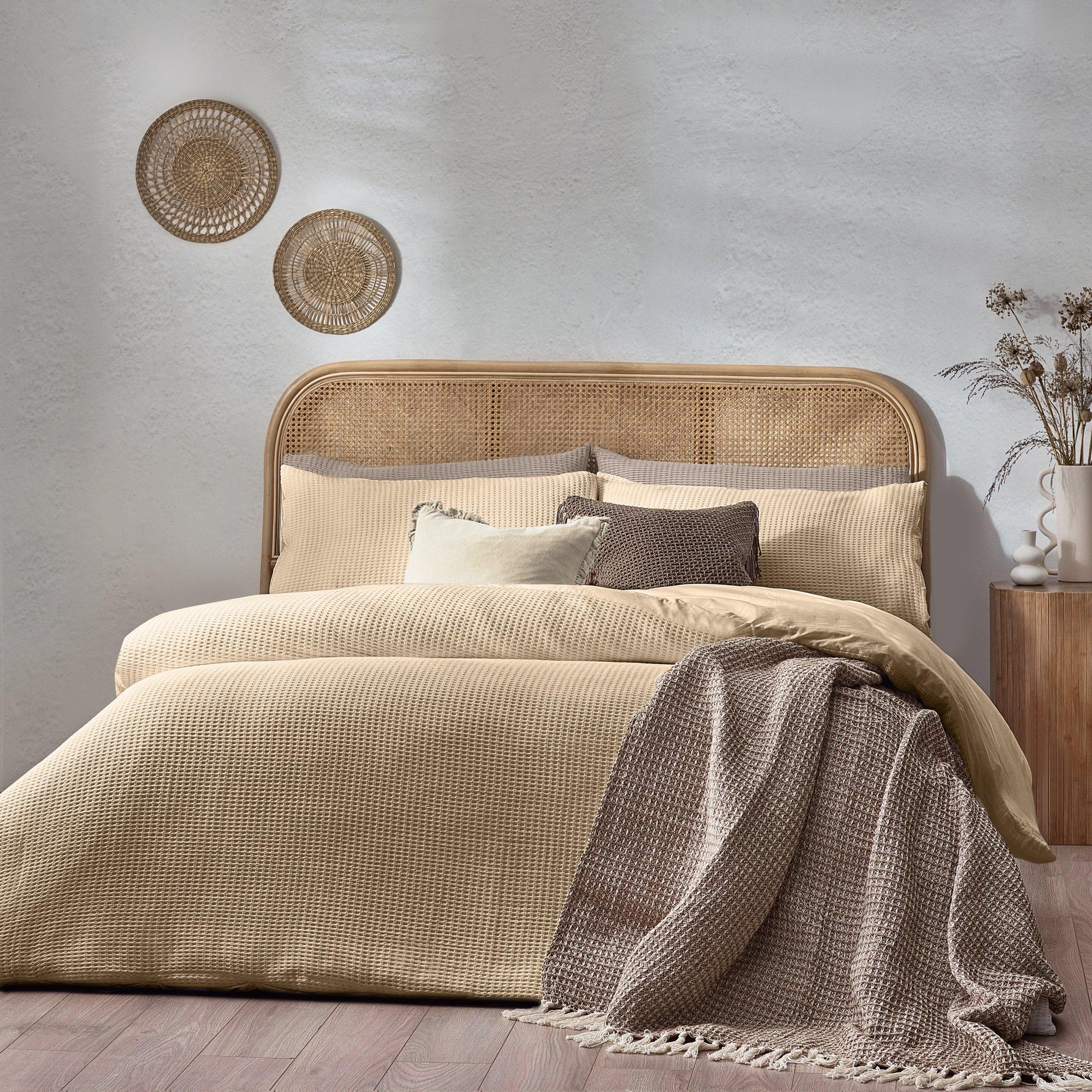 Chunky waffle textured duvet cover set in warm beige cotton, featuring matching pillowcases, styled with a cozy throw blanket and decorative wall hangings in a serene bedroom setting.