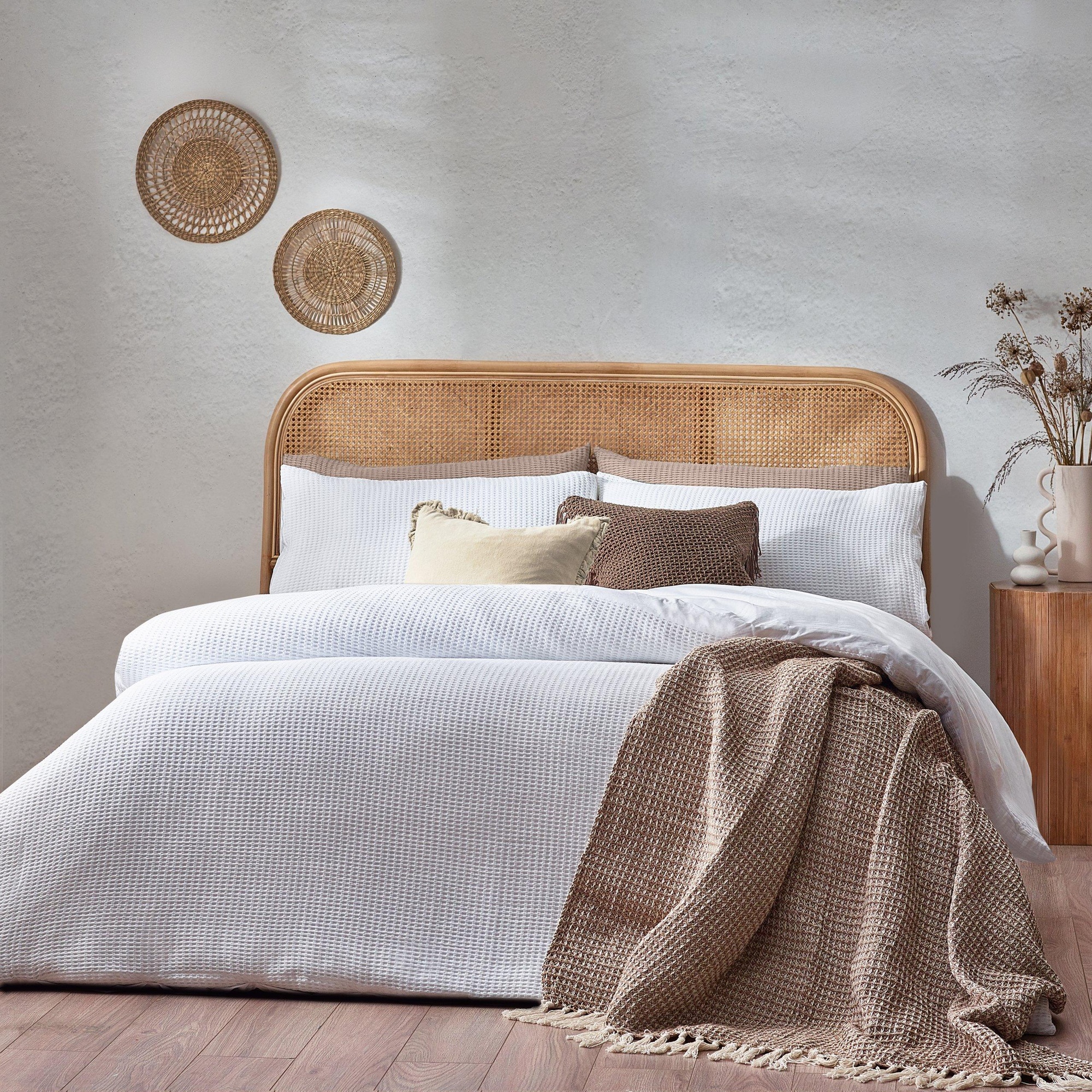 Chunky waffle textured white duvet cover set in king size, made of 100% cotton, styled with a beige throw and decorative pillows on a bed with a rattan headboard.