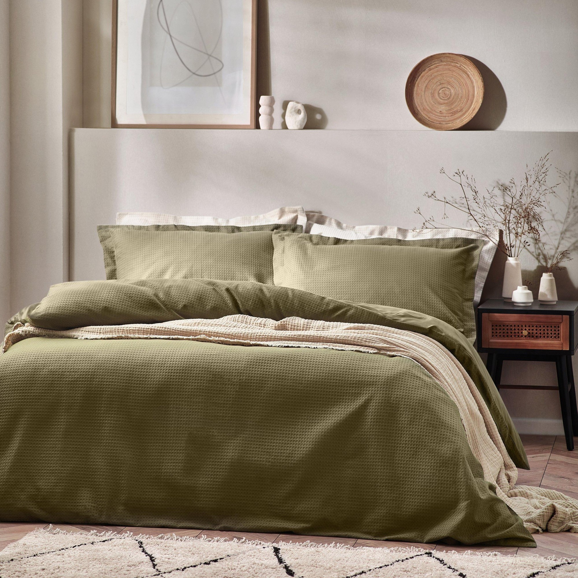 Green waffle textured duvet set with matching pillowcases, layered over a beige blanket, styled on a bed against a neutral wall and wooden decor.