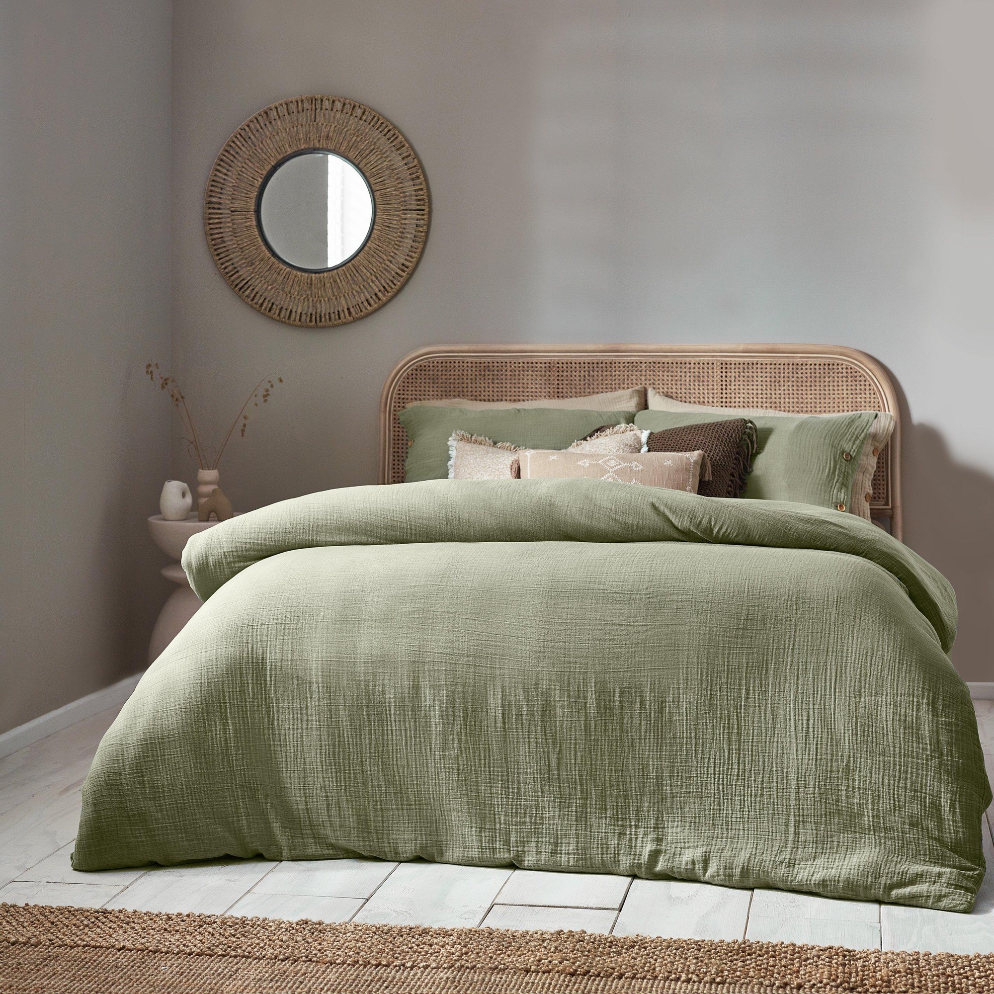 Green muslin cotton duvet cover set in super king size, featuring a textured finish, paired with neutral pillows, set against a soft-toned room with a round mirror and woven decor.
