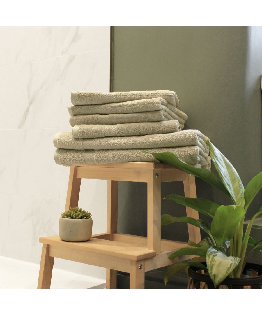Beige cotton hand towels and bath sheets stacked neatly on a wooden stool, with a small potted plant beside them against a green wall and marble background.