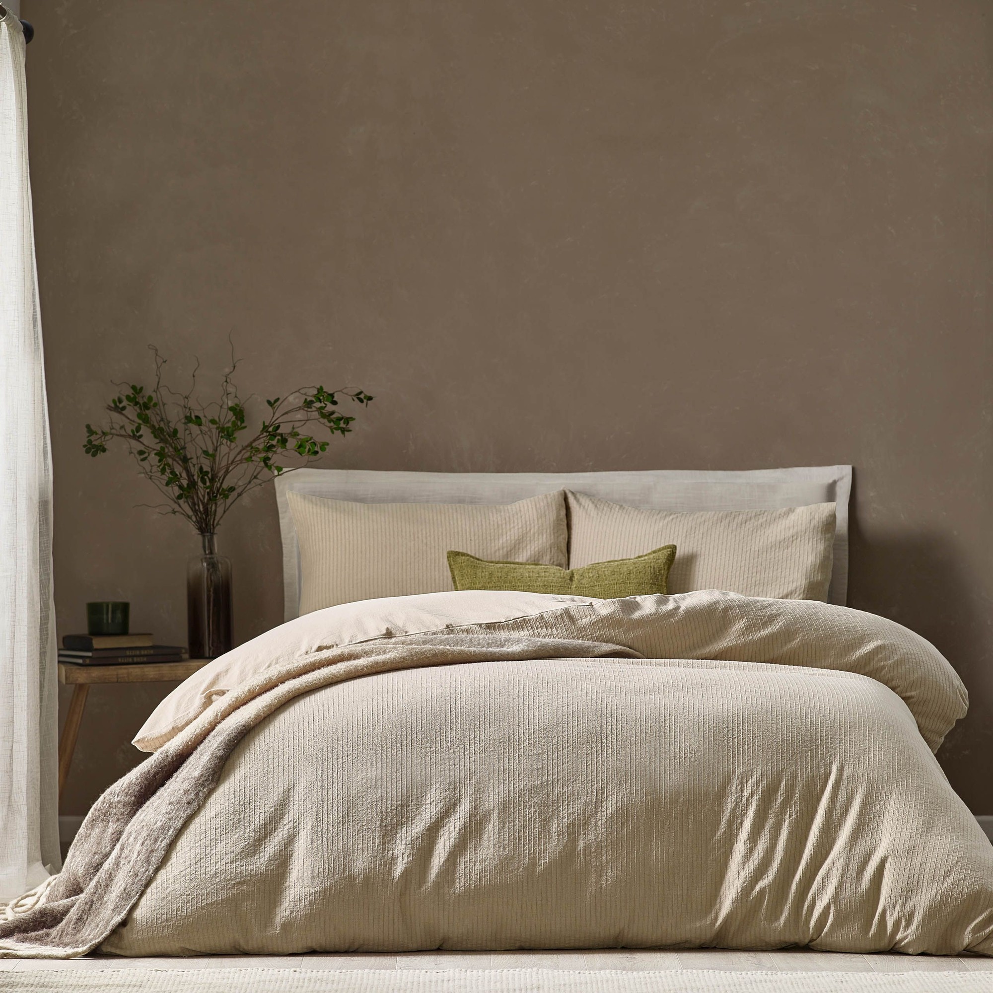Cream-colored 100% cotton single duvet cover set featuring a subtle Malton stripe pattern, complemented by a textured throw and green accent pillow against a neutral backdrop.