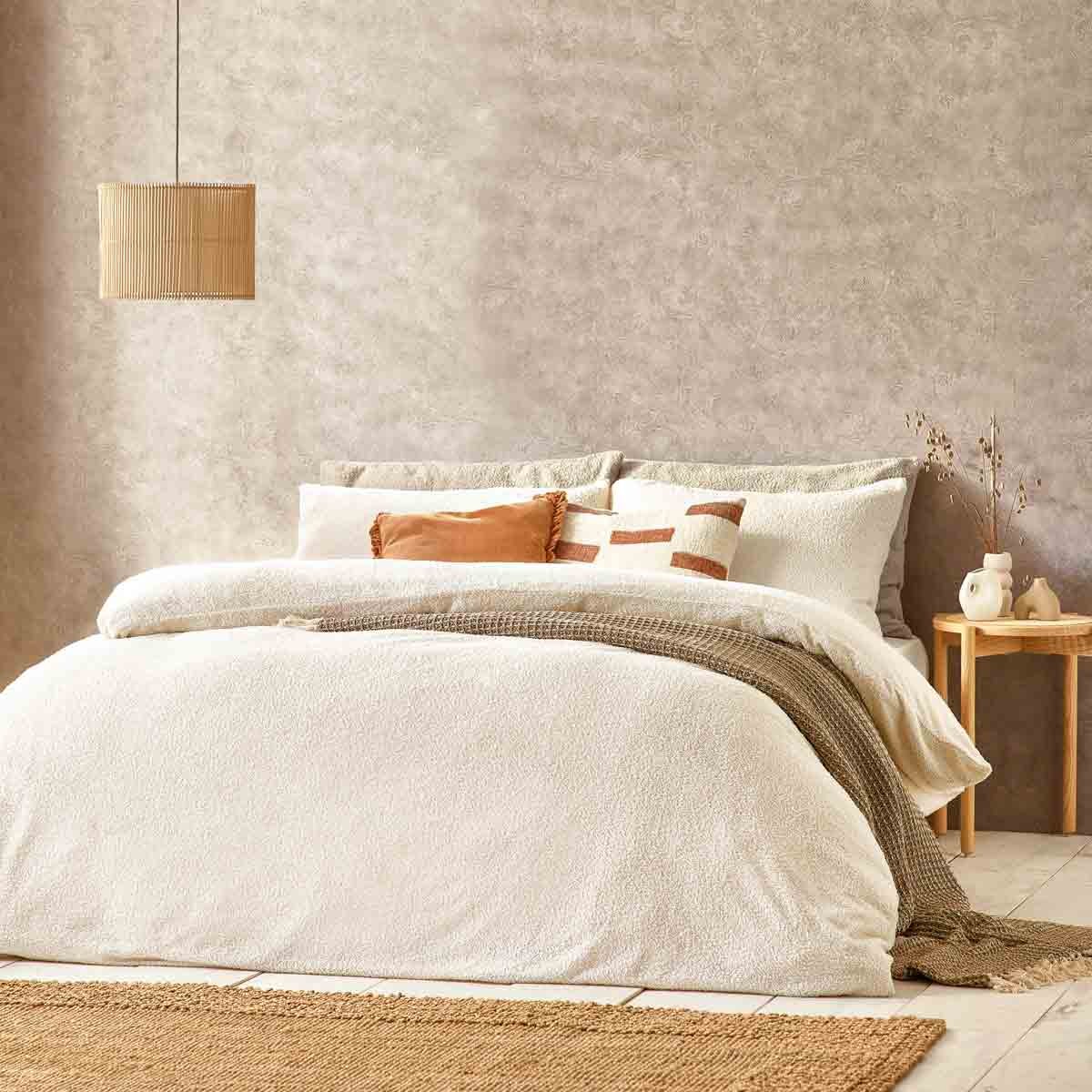 Cream boucle textured duvet set featuring a soft, cozy design, complemented by decorative pillows and a neutral color palette, set against a warm, textured wall and natural decor.