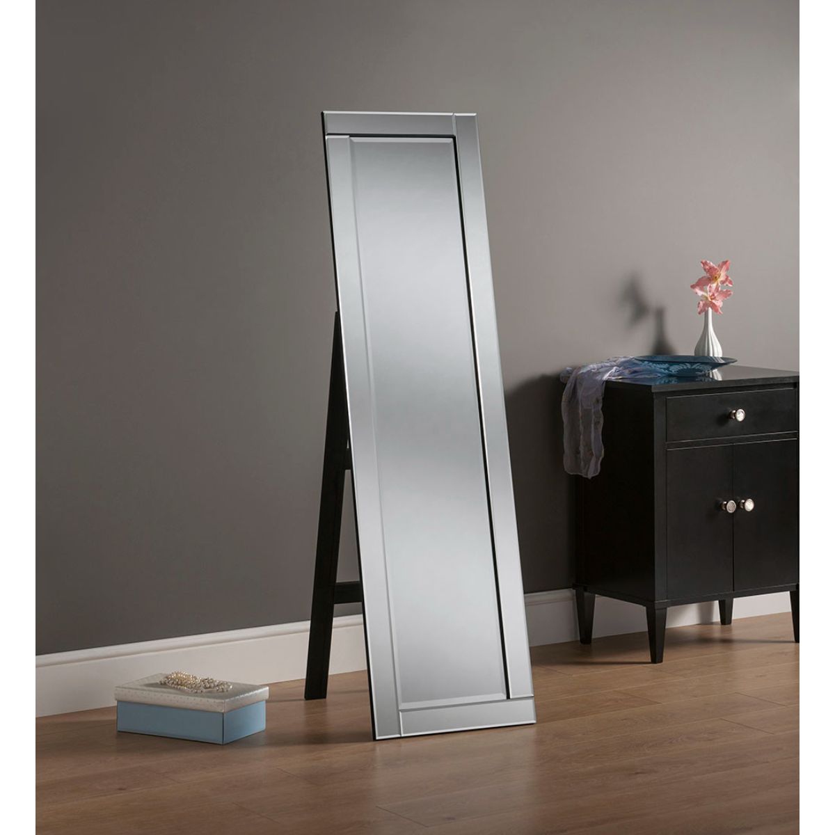Freestanding black cheval mirror with a bevelled edge, featuring a sleek design, positioned next to a black nightstand and a small decorative box on the floor.