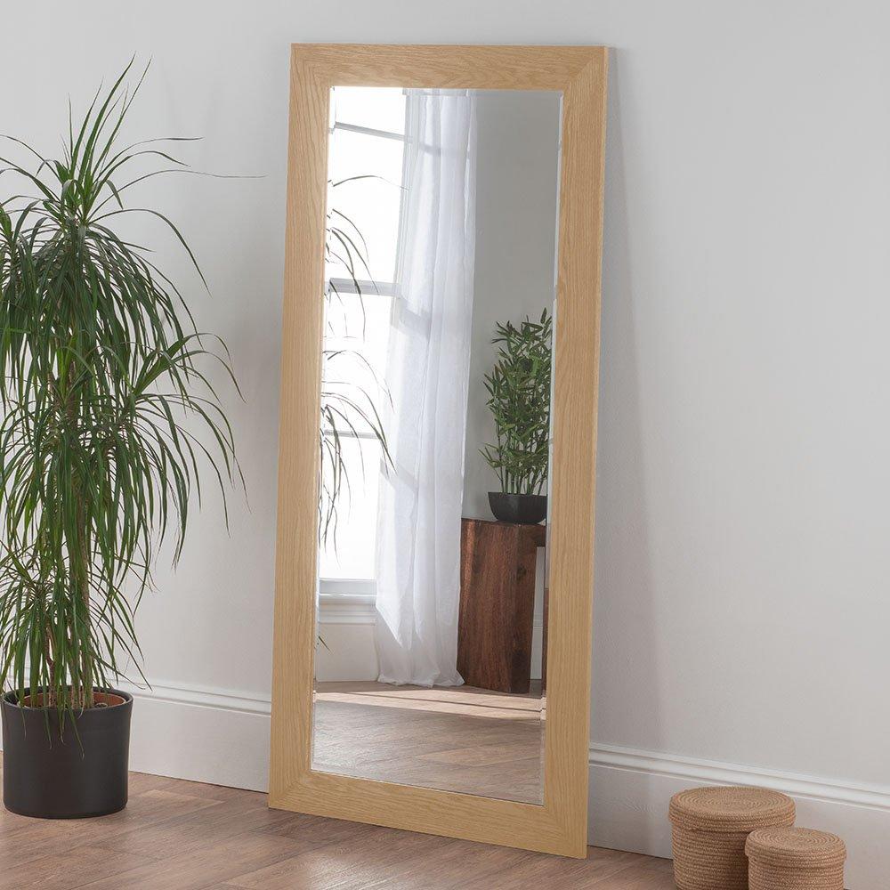 Tall, rectangular wall mirror with a natural oak effect frame, measuring 169.5x78cm, positioned beside a potted plant and woven baskets on a wooden floor.