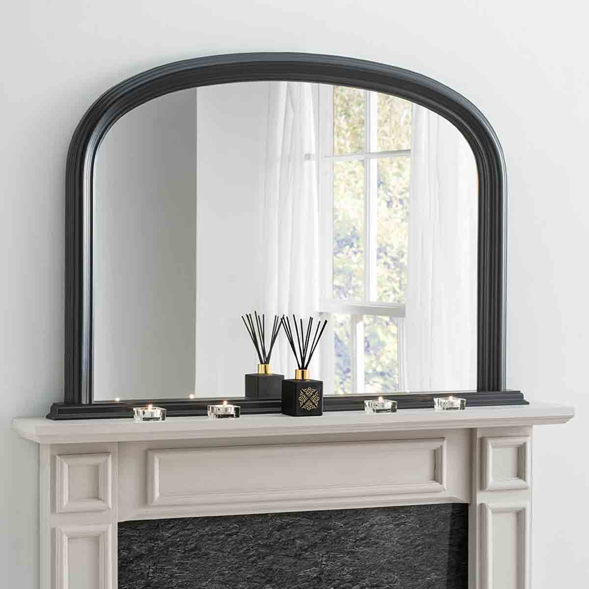 Arched contemporary black mirror with a sleek frame, measuring 112cm wide and 77cm high, displayed above a mantel with decorative candles and a diffuser.