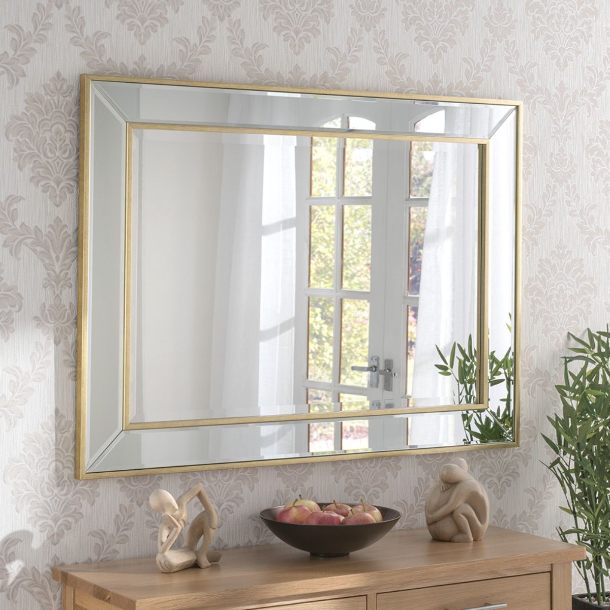 Rectangular angled wall mirror with a metallic gold brass frame, measuring 69.5x95cm, reflecting a light-filled room with decorative elements and a wooden console.