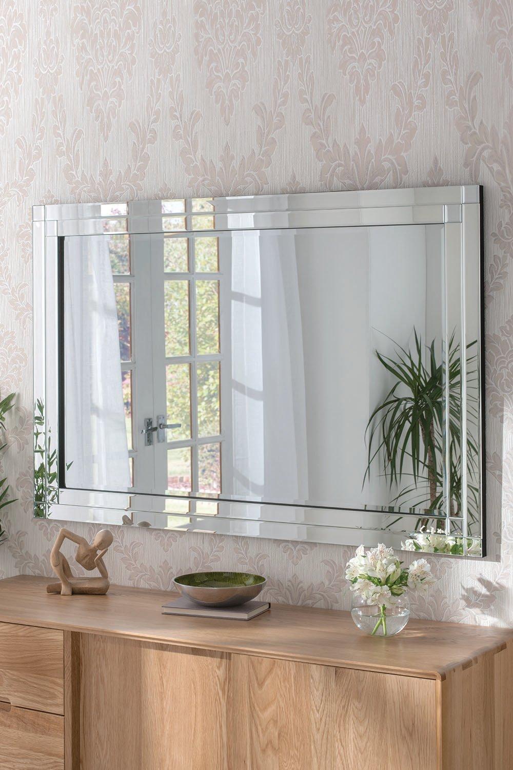 Double bevelled black wall mirror measuring 120x80cm, featuring a sleek frame that reflects light, positioned above a wooden console with decorative elements and plants.
