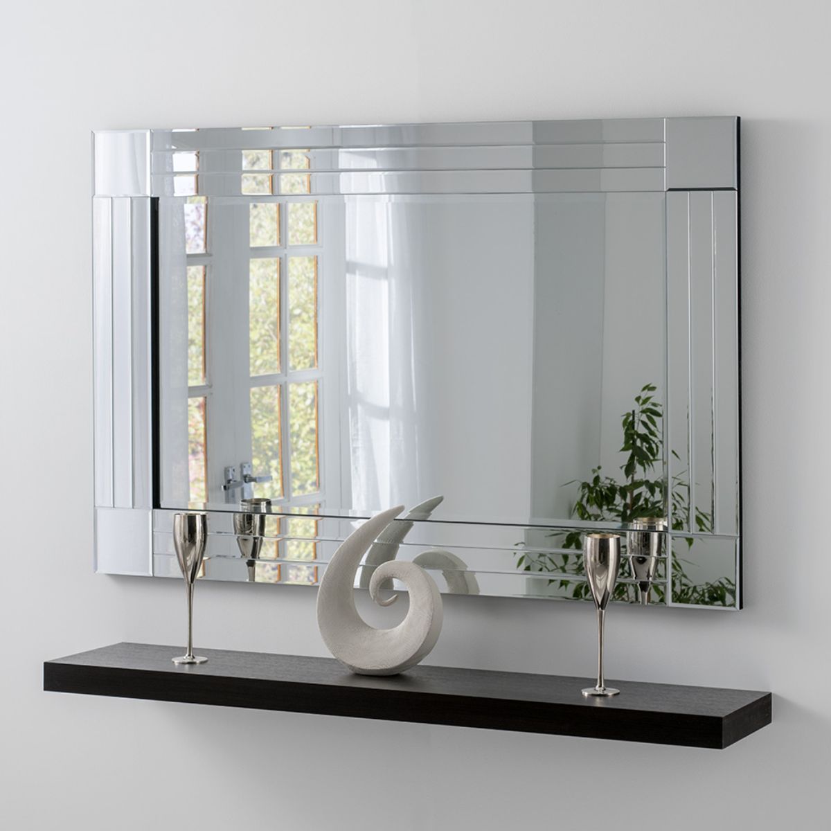 Bevelled triple edge mirror in black, measuring 120x80cm, featuring a sleek design with reflective surfaces and a minimalist shelf displaying a decorative sculpture and two silver glasses.