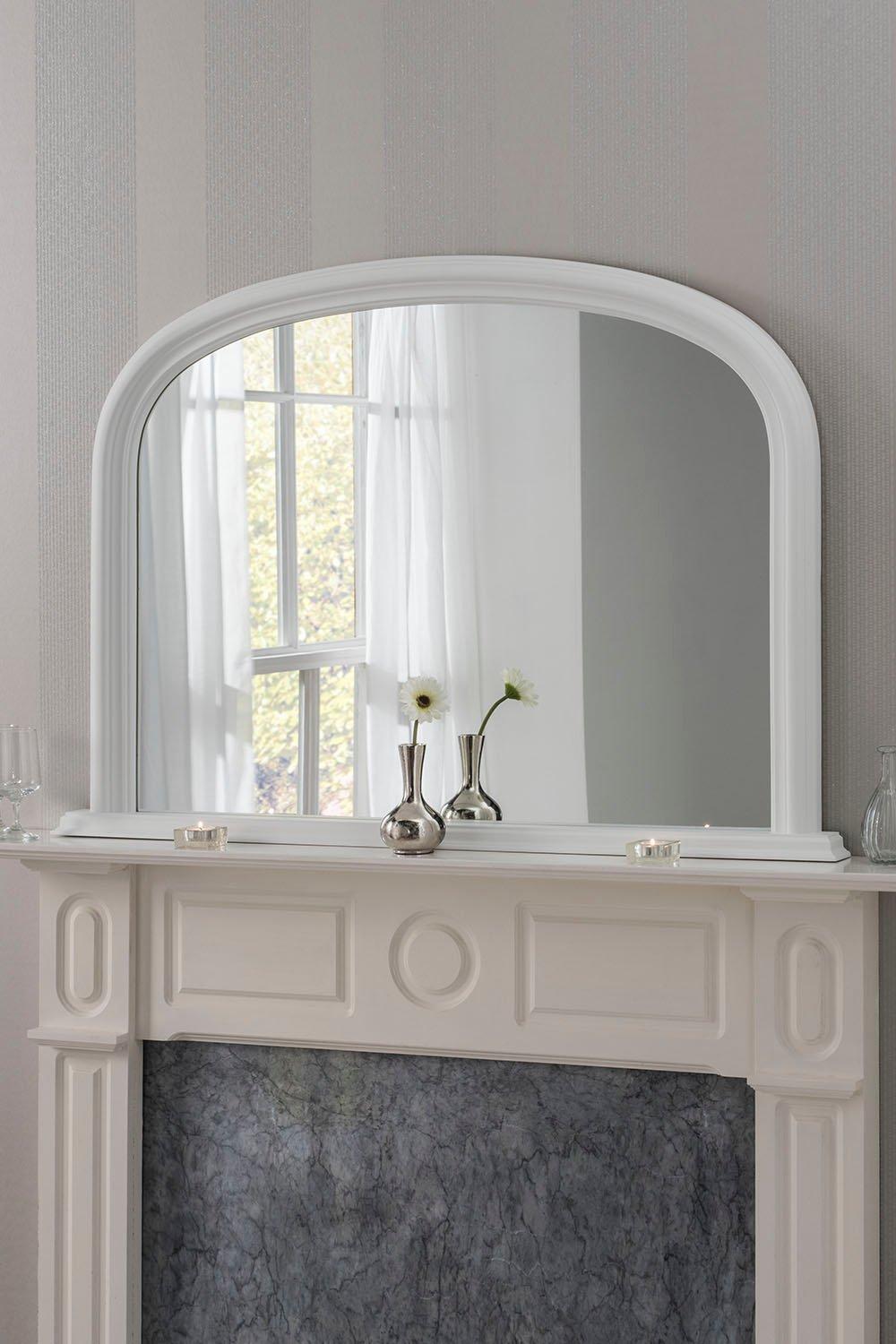 Arched contemporary mirror in white, measuring 112cm wide by 77cm high, reflecting light and decor above a stylish fireplace with a marble base.