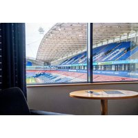 Bolton Stadium Hotel room with view of football pitch, featuring a round wooden table and dark chair by the window.