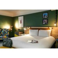 Hotel room with a large white bed, green walls, colorful armchair, and modern lighting fixtures.