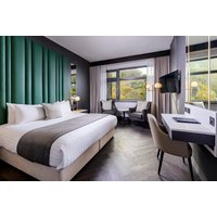 Luxury hotel room with king bed, green accent wall, desk, TV, and large windows overlooking greenery.