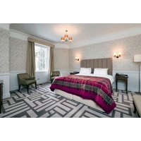 Elegant hotel room with a king-sized bed, plaid throw, patterned carpet, and classic decor at Atholl Palace Hotel.