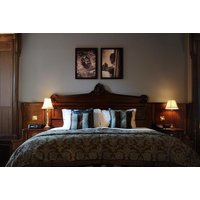 Luxurious hotel room with ornate wooden headboard, plush bedding, decorative pillows, and warm bedside lamps.