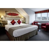 Radisson Blu Durham room with double bed, red cushions, striped bed skirt, armchairs, window view, and bedside lamps.