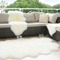White sheepskin double rug on patio floor, draped over wicker sofa, with plush texture and natural shape.