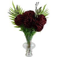 Red Chrysanthemum artificial flowers in a clear glass bubble vase with green fern leaves and purple accents.