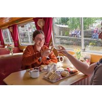 Afternoon tea set with sandwiches, scones, pastries on a wooden table in a cozy cafe with red curtains.