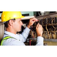 Electrician wearing yellow hard hat and safety vest working on a complex electrical panel with multiple wires.