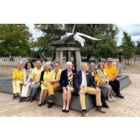 Group of people in yellow attire sitting on a stone sculpture with a large bird in a park setting.
