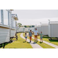 Family walking between white caravans at Flower of May Holiday Park, Yorkshire, with green lawns and clear skies.