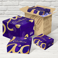 Purple Cadbury gift box set with gold accents, open cardboard box, and smaller matching boxes on white wood surface.