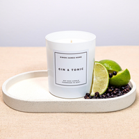 Handmade white soy wax candle labeled "Gin & Tonic" with lime and juniper berries on a ceramic tray.