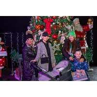 Family at Gulliver's World with stroller, standing by a large decorated Christmas tree and Santa statue, festive lights.