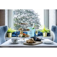 Hotel Colessio breakfast setup with pastries, tea, Prosecco, and tiered tray by a window with plants.