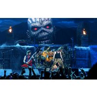 Band performing on stage with large monster backdrop, red-eyed skull, guitarist in red, and drummer in center.