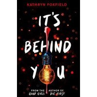 Black book cover "It's Behind You" by Kathryn Foxfield, features a glowing lightbulb with red paint dripping.