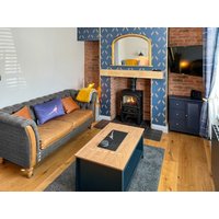 Cozy living room with blue sofa, wooden coffee table, brick fireplace, wood-burning stove, and patterned blue wallpaper.