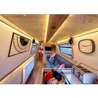 Luxurious narrowboat interior with wooden paneling, ambient lighting, plush seating, wall art, and a large clock.