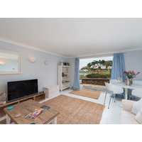 Coastal-themed living room with large window, blue curtains, TV, wooden coffee table, and wicker rug.
