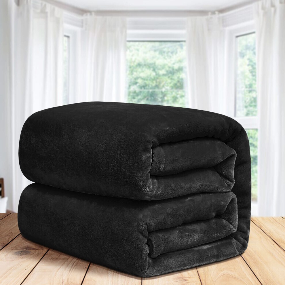 Soft, plush black fleece double blanket stacked on a wooden surface, with sunlight filtering through sheer curtains in the background.