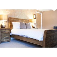 Cozy hotel room with wooden bed frame, white bedding, two bedside tables with lamps, and neutral-toned walls.