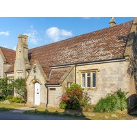 Stone cottage with pitched roof, arched doorway, and chimney, surrounded by greenery under a blue sky.