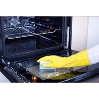 Open oven with yellow-gloved hand cleaning interior using a blue sponge, showcasing professional cleaning service.