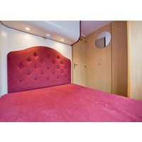 Red upholstered headboard with tufted design in a cozy room, wooden walls, and circular mirror.