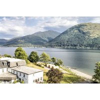 Scottish Highlands hotel by a lake with mountain views, featuring white buildings and lush greenery.