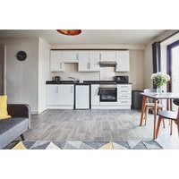 Modern studio apartment with white cabinets, compact kitchen, dining table, and sofa, featuring wood flooring.