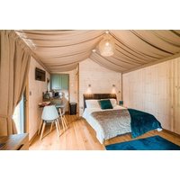 Cozy wooden cabin interior with double bed, draped ceiling, small kitchenette, and seating area.