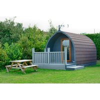 Wooden glamping pod with arched roof, front porch, and picnic table set in lush green countryside.