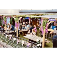Outdoor seating area at Bar 50, Edinburgh, with wooden tables, floral decorations, and patrons enjoying small plates and cocktails.