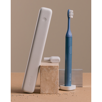 Blue SURI 2.0 Sonic Electric Toothbrush with white bristles and sleek white case, standing on beige blocks.