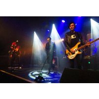 Band "The Damned" performing on stage with colorful lights and instruments, guitarist in leather jacket playing electric guitar.