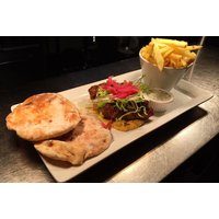 Rectangular plate with flatbreads, a burger topped with lettuce and red onions, fries in a cup, and a small sauce dish.