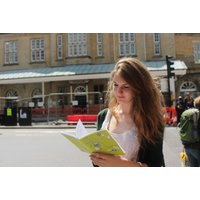 Woman holding a green map booklet for Treasure Hunt Themed City Walking Tours by Curious About, standing outdoors.